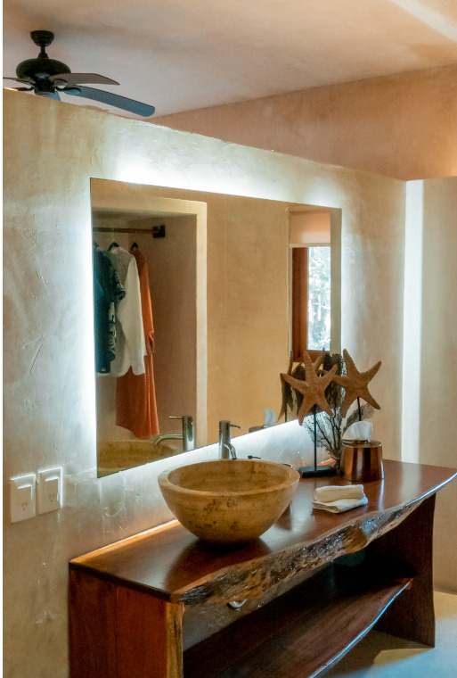Luxury bathroom vanity at Cachito de Cielo Tulum featuring a stone vessel sink on a live-edge wooden counter, backlit mirror, and decorative starfish