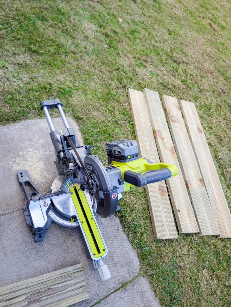 Four cut decking board pieces laid out on the grass next to the mitre saw ready for assembly