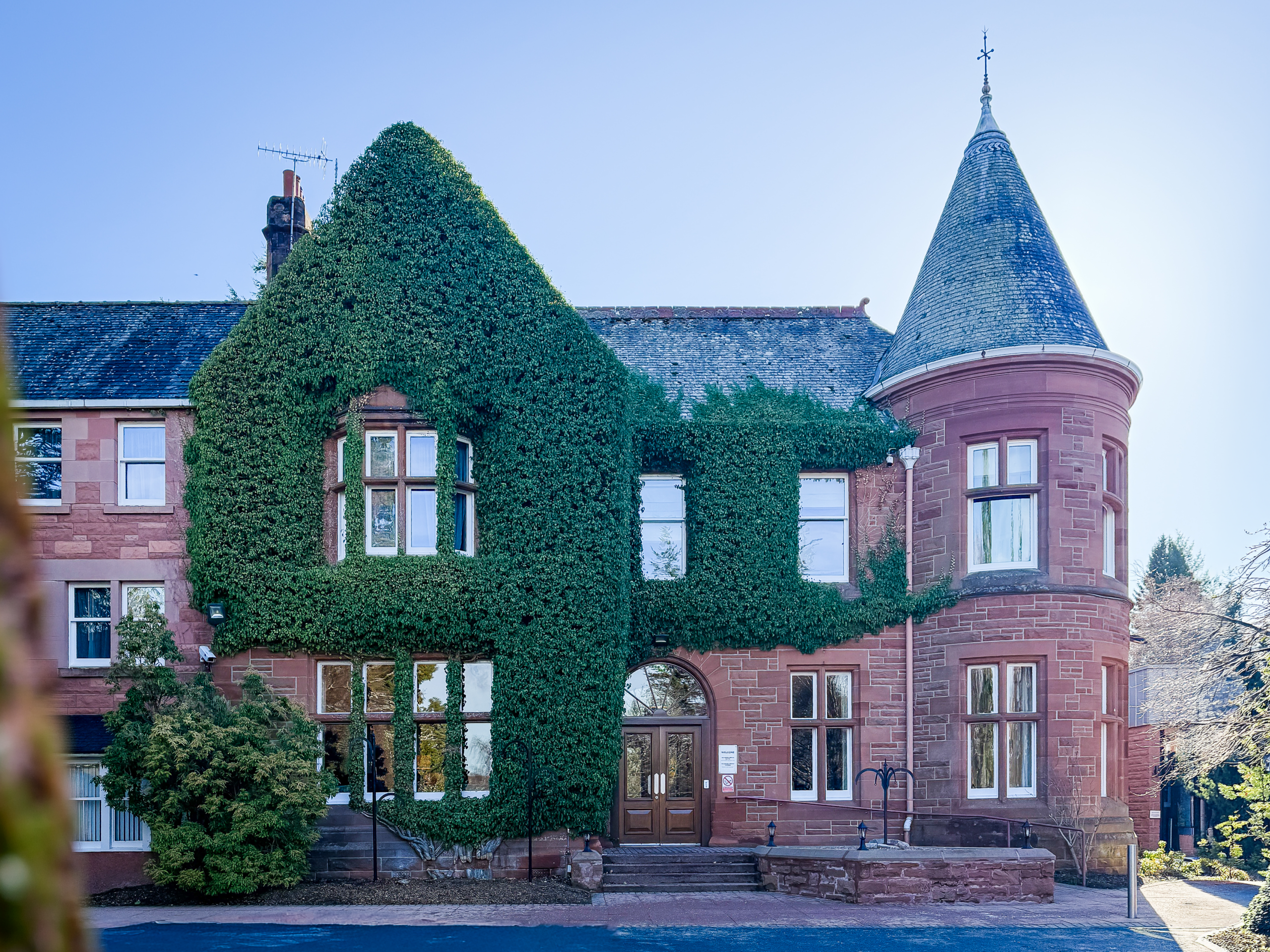 Craigendarroch Hotel & Spa covered in dense ivy, with a pointed turret and blue sky above
