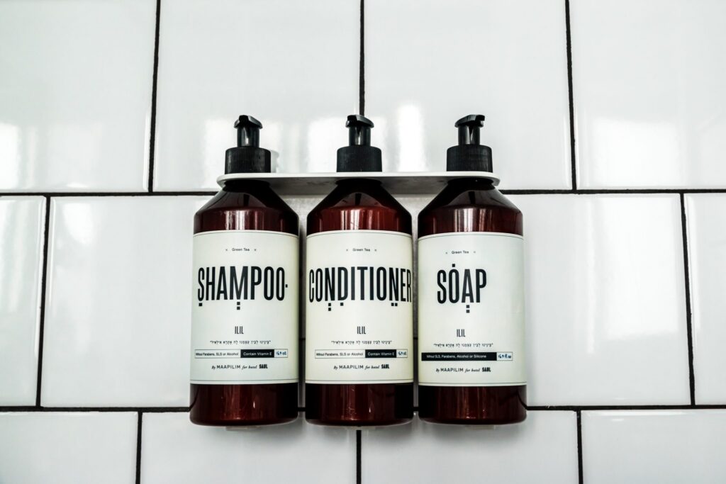 Three amber pump bottles of MAAPILIM shampoo, conditioner and soap made exclusively for Hotel Saul, mounted on white subway tiles