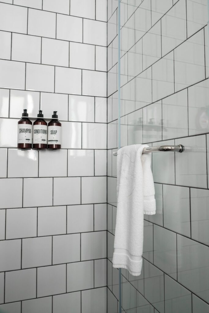The rain shower at Hotel Saul Tel Aviv, with white subway tiles, black grout, MAAPILIM toiletries on a built-in shelf, and a fluffy white towel