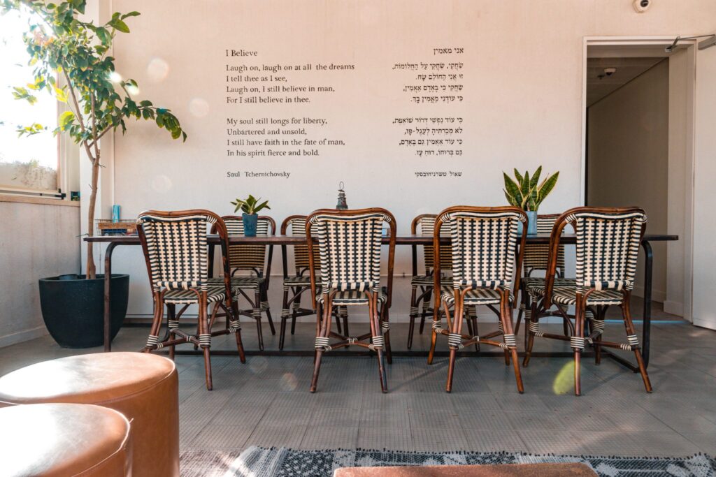 The covered terrace at Hotel Saul Tel Aviv, with wicker bistro chairs around a long dining table and a poem printed on the white wall