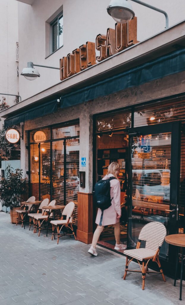 The exterior entrance of Hotel Saul Tel Aviv, with the illuminated Hotel Saul sign above the door and pavement café tables outside