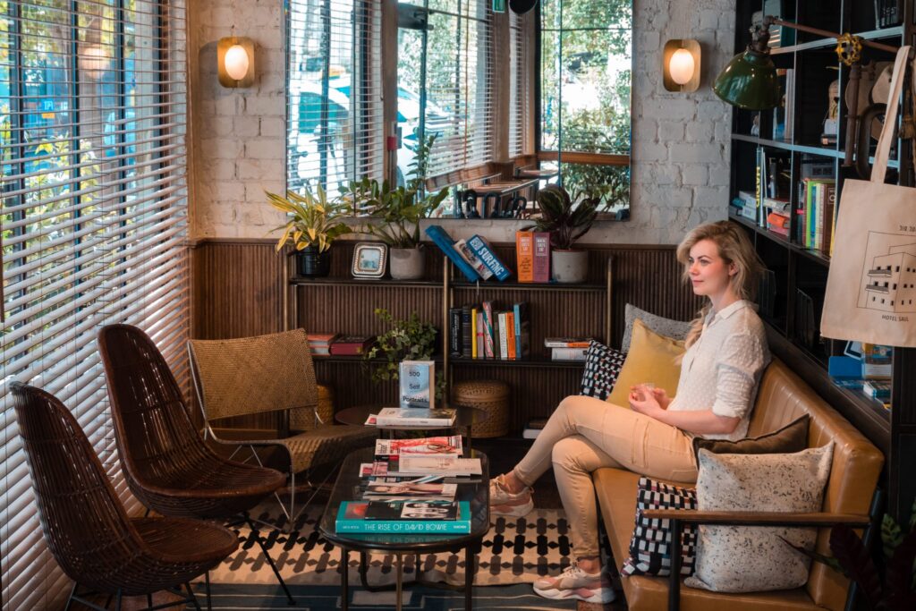 A woman relaxing in the boutique lobby reading nook at Hotel Saul Tel Aviv, surrounded by books, plants, and mid-century style furniture