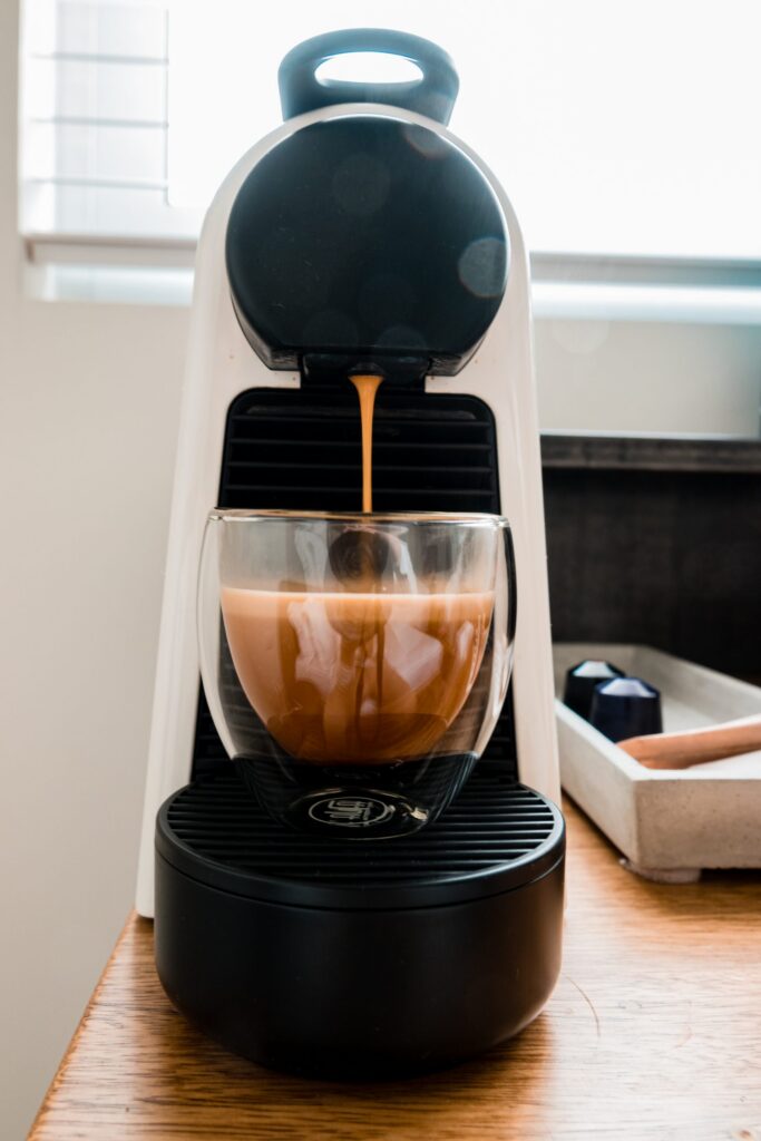 A Nespresso machine brewing coffee into a glass cup in a Hotel Saul Tel Aviv guest room, with capsules in a tray alongside