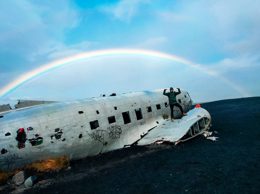 The iconic DC3 plane wreck on Iceland's black sand beach with a full rainbow overhead