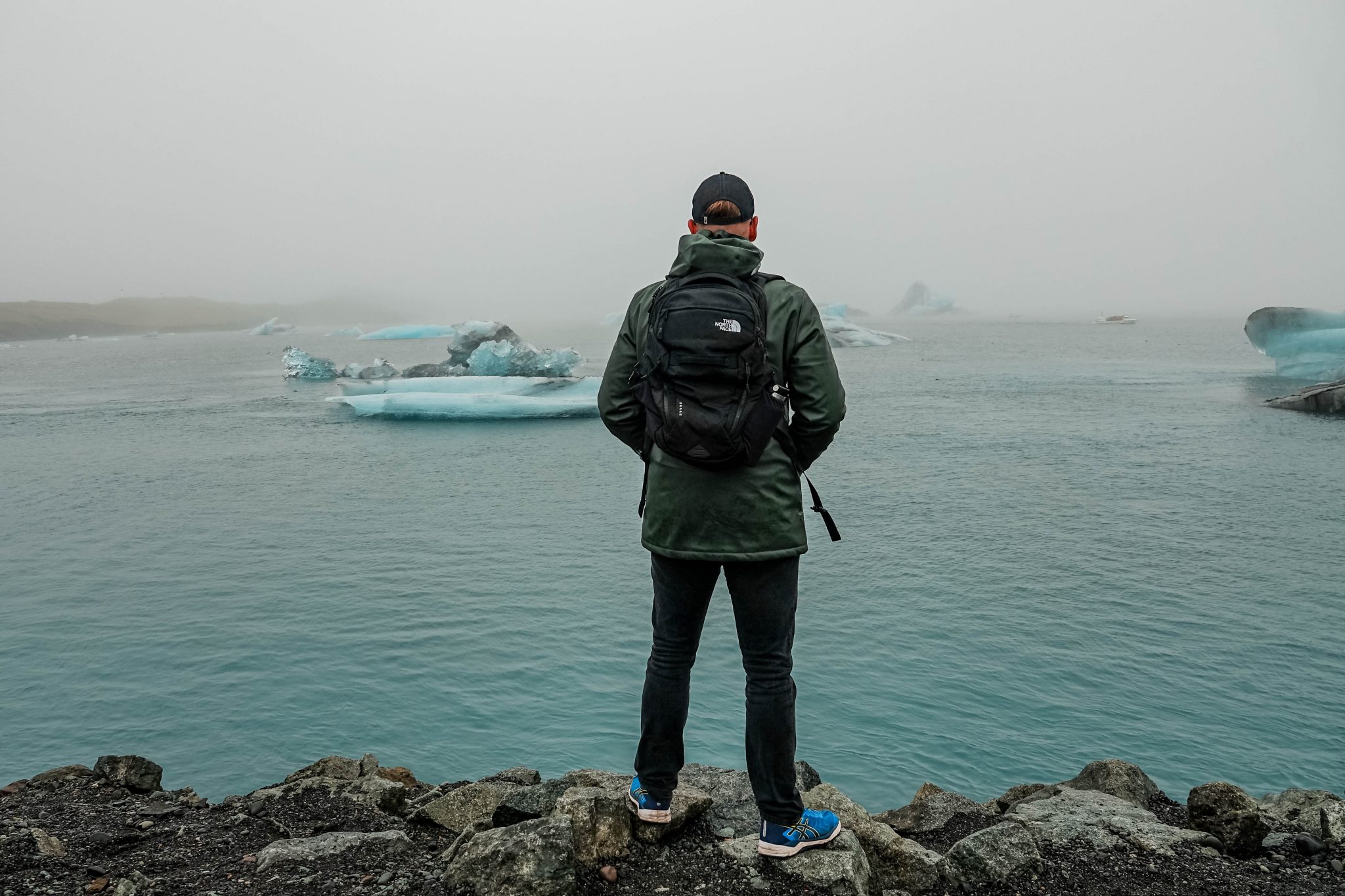 Person with backpack standing at the edge of Jökulsárlón glacier lagoon surrounded by floating ice in fog