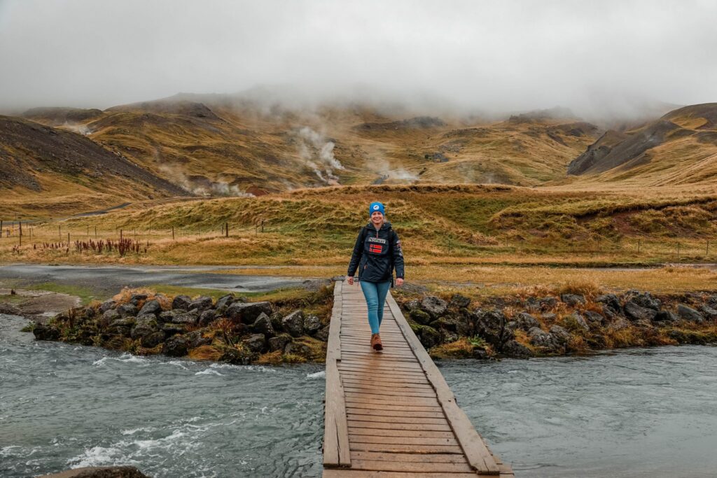Woman crossing a wooden footbridge over a glacial river on the Reykjadalur hot spring hike, Iceland