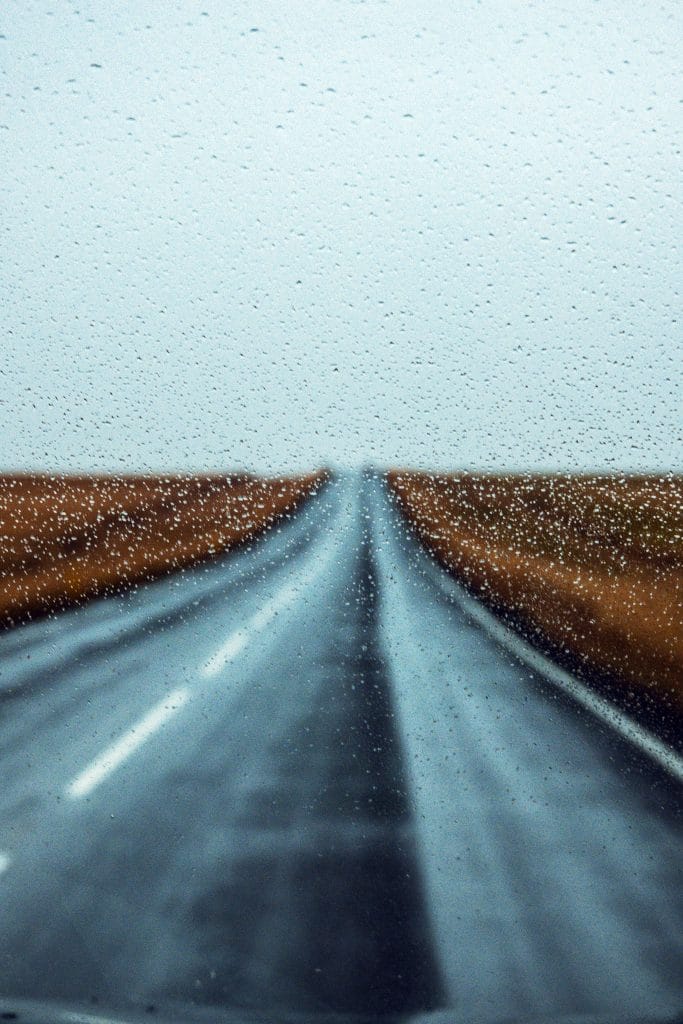 View through a rain-covered windscreen of Iceland's straight Route 1 stretching into the distance