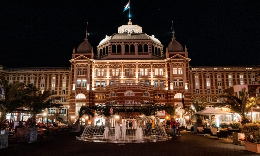 Grand Hotel Amrath Kurhaus lit up at night with an ornate fountain in the foreground, Scheveningen