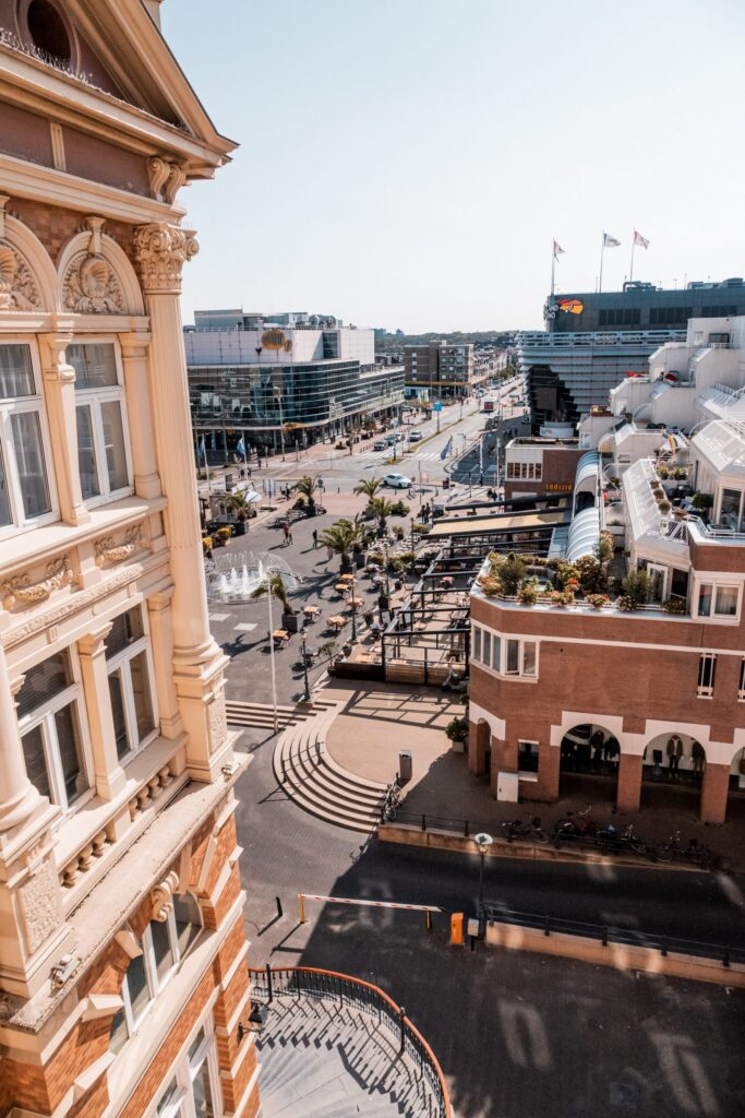 View from a Kurhaus hotel room window looking down onto the Scheveningen promenade, with palm trees, fountains and the town square