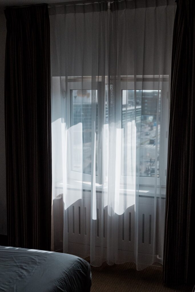 Sheer curtains in a Kurhaus hotel room diffusing daylight, with city views visible through the window