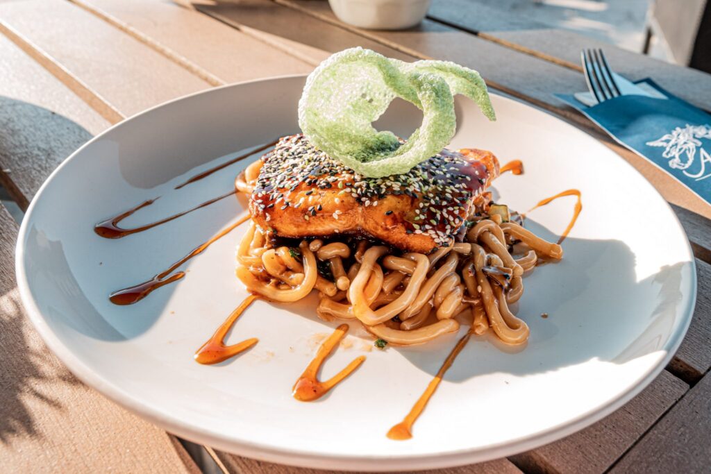 Sesame-crusted salmon on noodles with a crispy green garnish, served at Waves restaurant at the Kurhaus Scheveningen