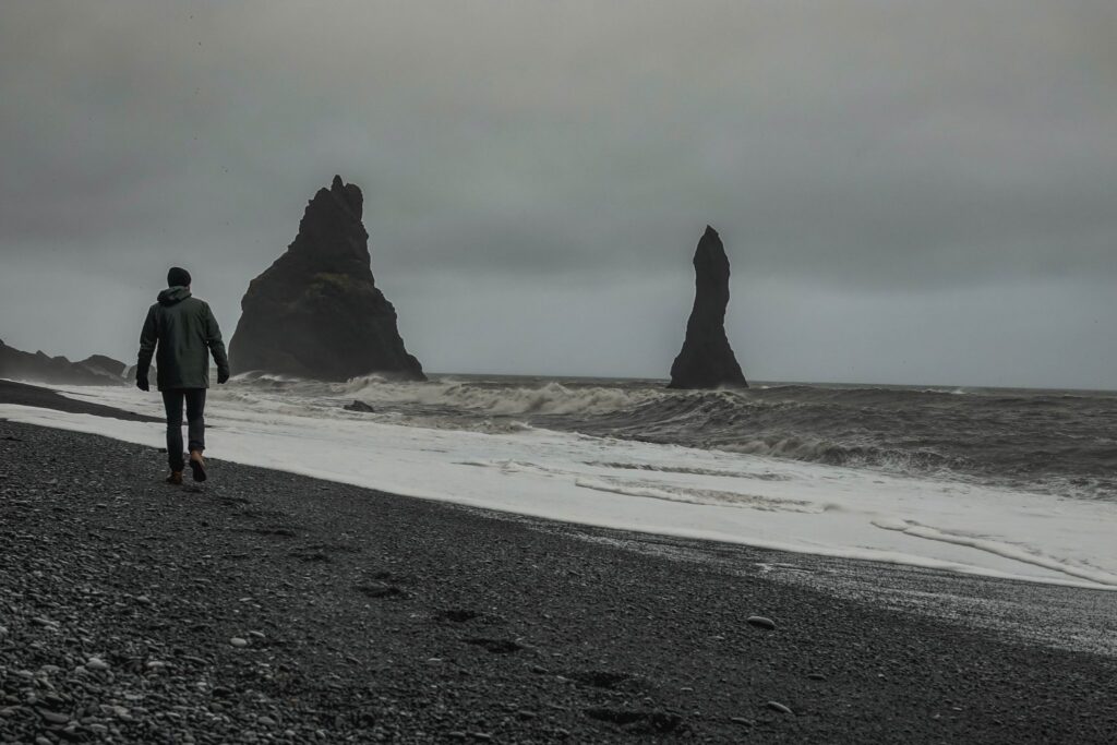 Person walking along Reynisfjara black sand beach with dramatic basalt sea stacks in grey mist