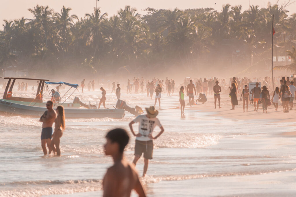 Busy Tulum beach packed with tourists in golden hour haze, showing how crowded it gets