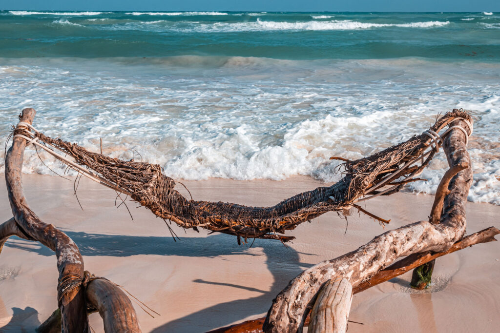 Rustic driftwood hammock sculpture on Tulum beach with turquoise Caribbean sea in the background