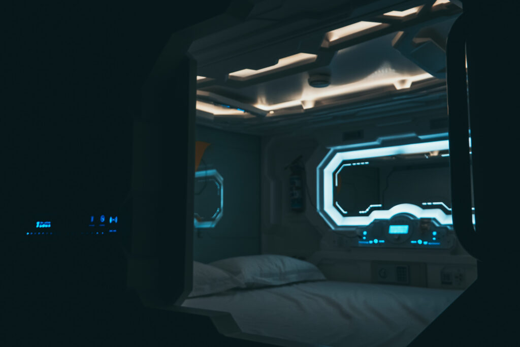 Inside view of a sci-fi style capsule pod at the Yellow Capsule hotel Cancun, with glowing blue lights and a porthole window