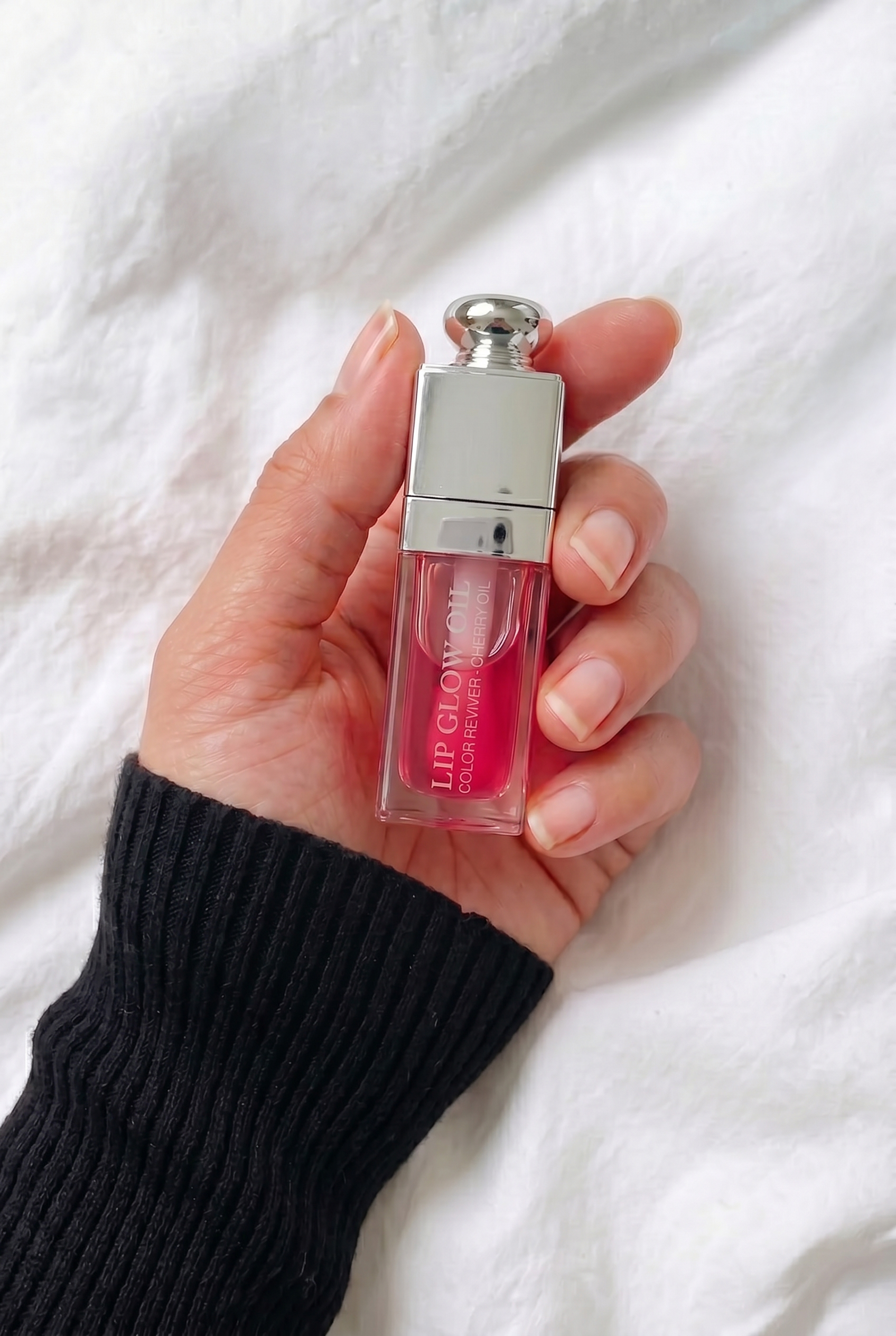 A person holding the Dior Lip Glow Oil in their palm against a white fabric background to show the compact scale of the 6ml luxury packaging.