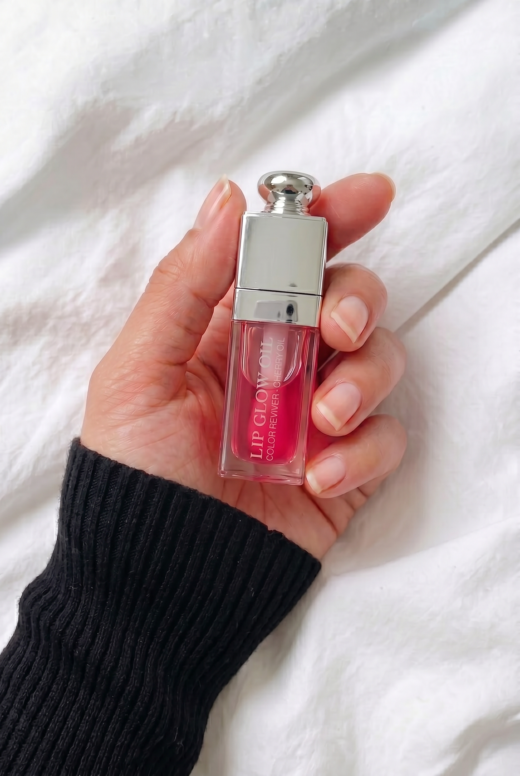 A person holding the Dior Lip Glow Oil in their palm against a white fabric background to show the compact scale of the 6ml luxury packaging.