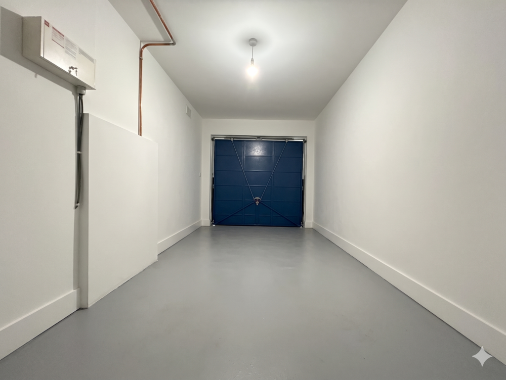 Cleared out UK garage with freshly painted white walls, a grey concrete floor and a blue up and over garage door, ready for the home gym conversion to start