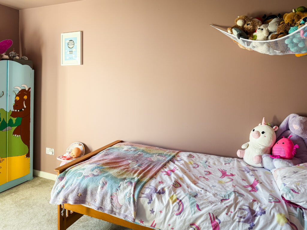 children's bedroom showing painted wardrobe soft toy hammock and wooden bed against sulking room pink walls