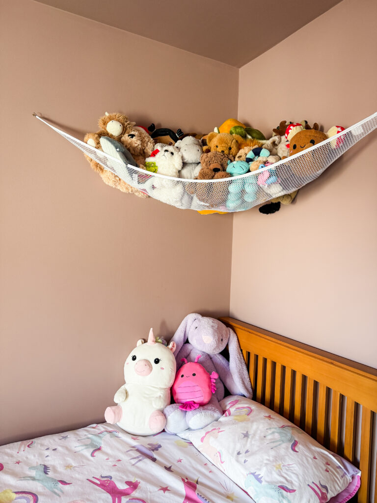 white mesh corner hammock filled with soft toys above a wooden bed in a sulking room pink bedroom