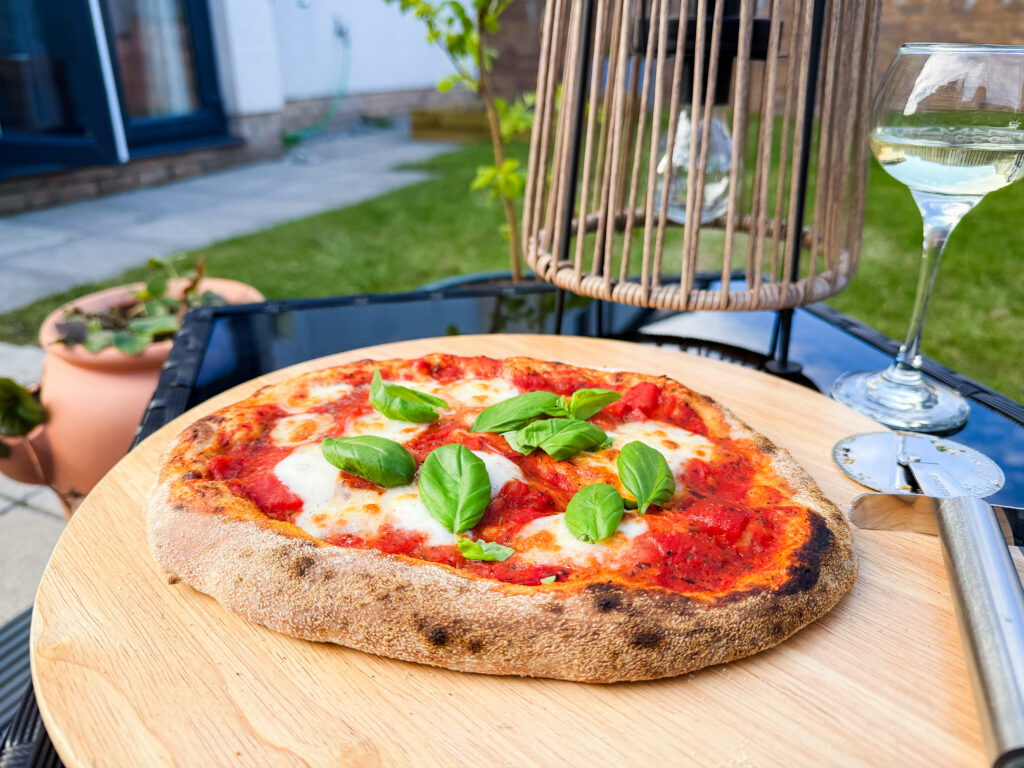 A vibrant close-up of a wood-fired margherita pizza with fresh green basil leaves on a wooden serving board.