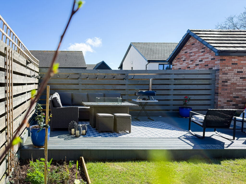 Outdoor living space featuring a grey sectional sofa, a tabletop pizza oven on a stand, and blue ceramic planters.