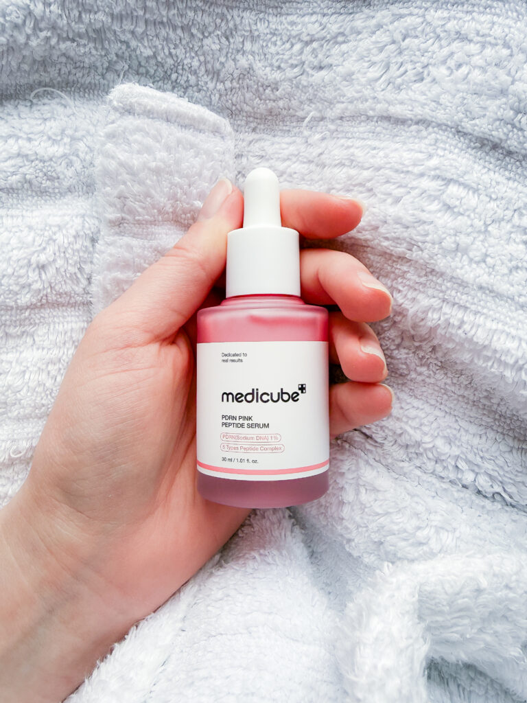 Close-up of Medicube PDRN Pink Peptide Serum 30ml bottle held against a white towel, showcasing the professional packaging and pink serum hue.