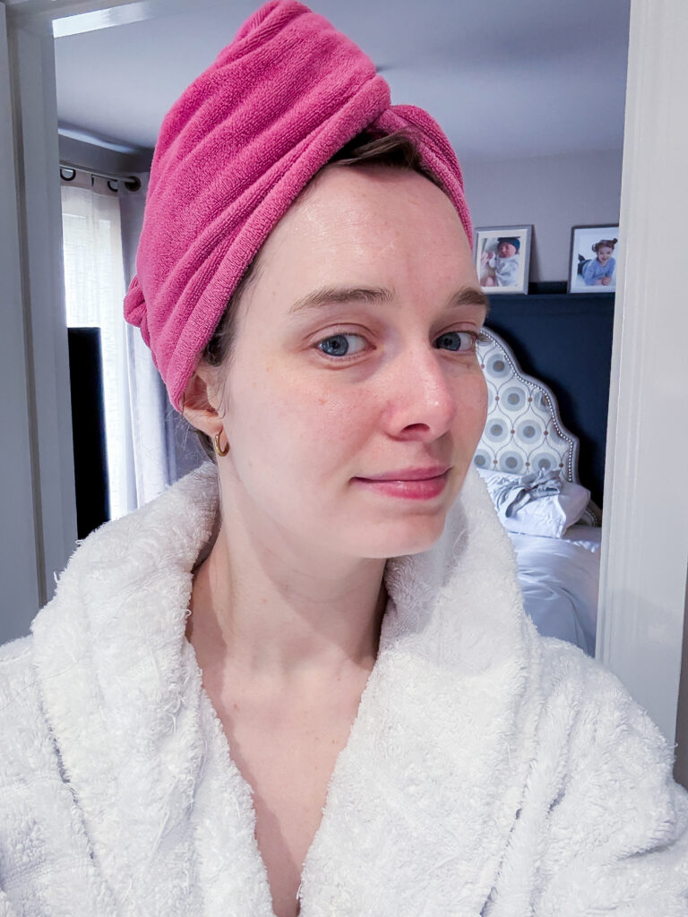 A 32-year-old woman with a glowing, hydrated complexion wearing a white robe and pink head towel after using the Medicube PDRN Pink Peptide Serum.