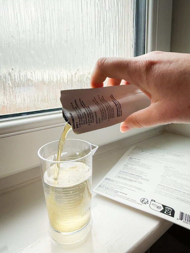 Pouring Olaplex No. 1 Bond Multiplier into a measuring cup with water for the stand-alone treatment dilution.