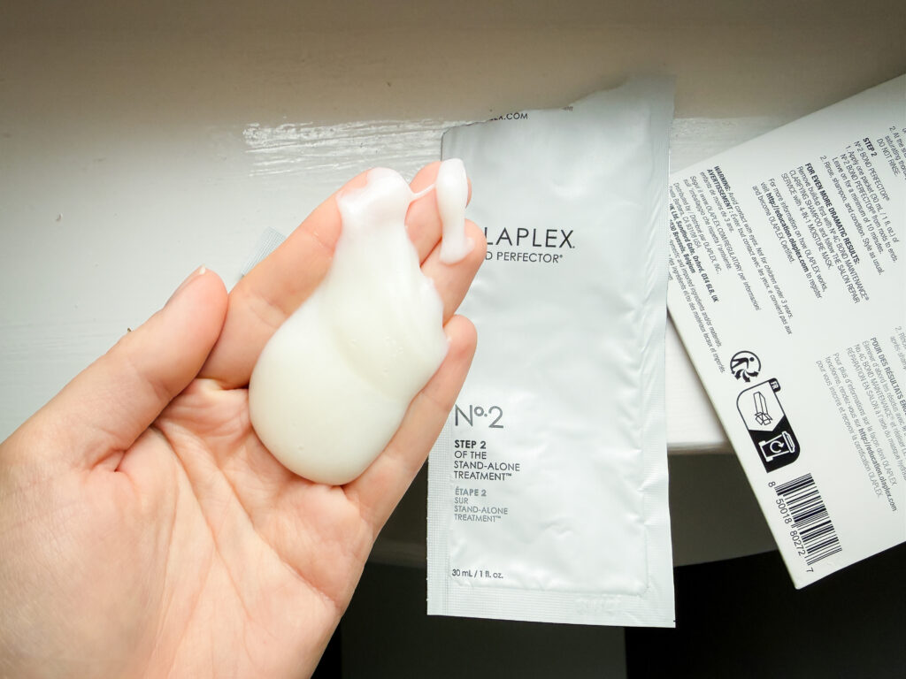 Close-up of Olaplex No. 2 Bond Perfector creamy consistency on hand with the professional sachet in the background.