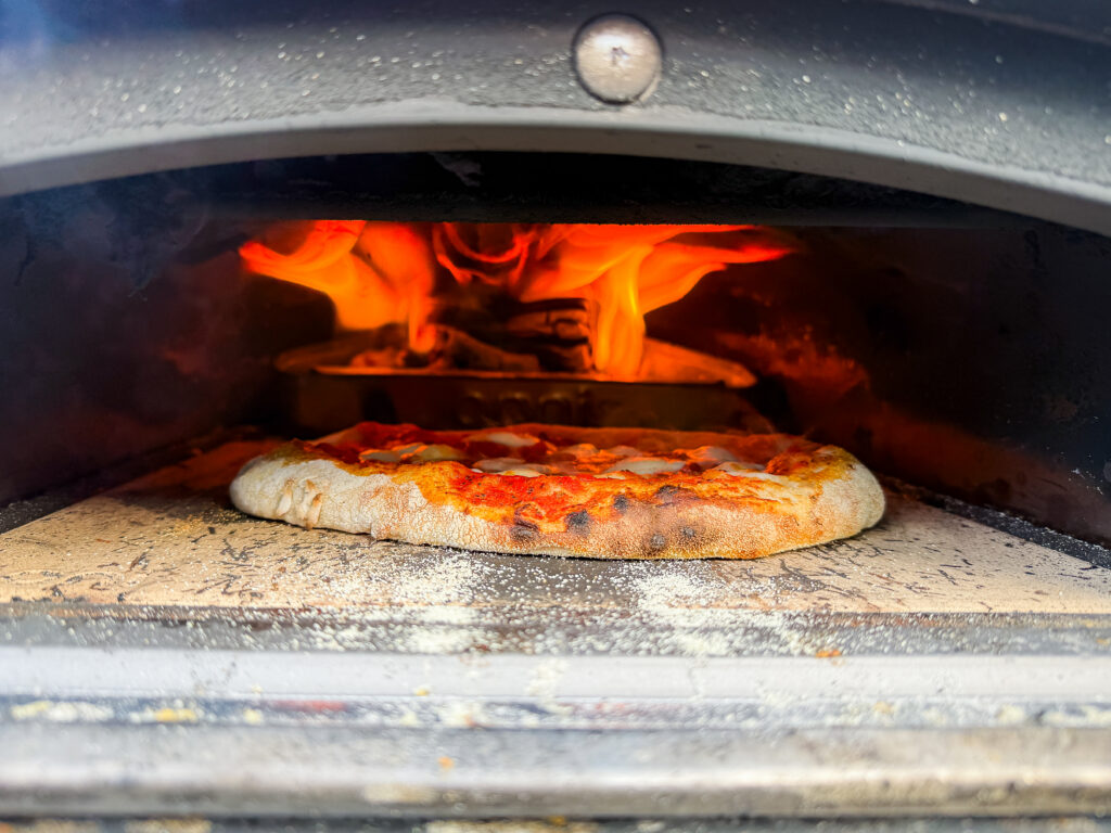 A margherita pizza cooking inside the Ooni Karu 2 with vibrant orange flames licking the roof of the oven.