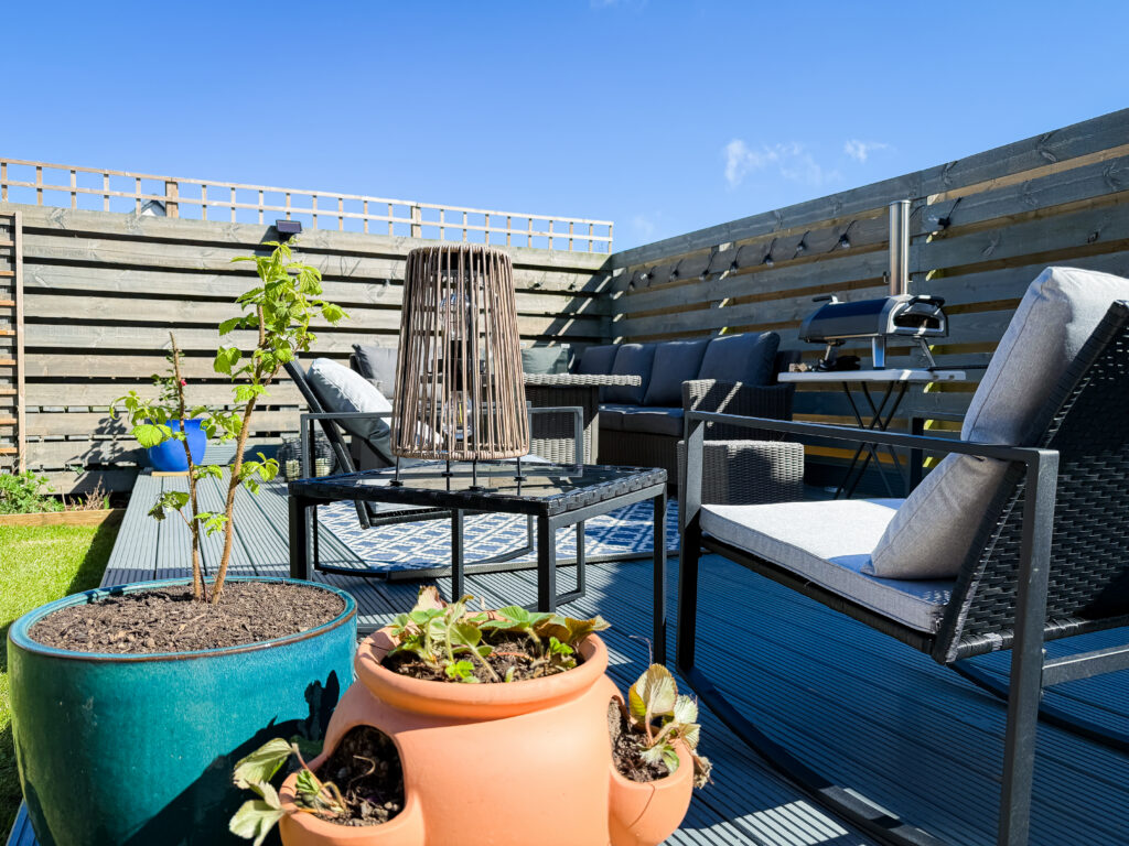 A wide shot of the garden lounge area including a terracotta strawberry planter and a tall wooden lantern.