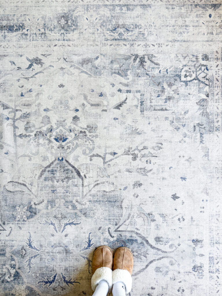 Top-down view of the Ruggable Sarrah Blue Quartz rug in a UK home, showing the intricate blue and cream pattern with someone wearing tan slippers for texture comparison.
