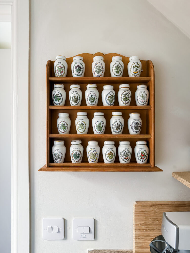 vintage ceramic spice jar collection on a wooden wall rack mounted against faux limewash painted walls