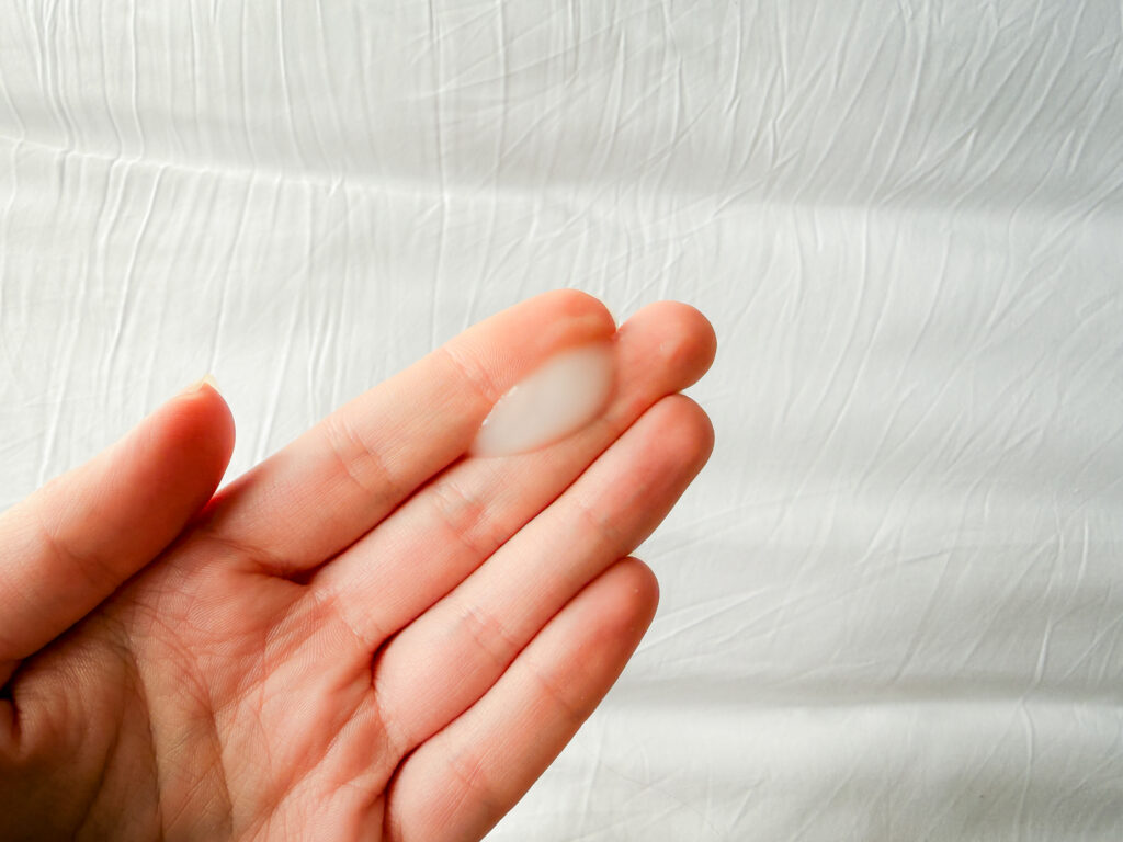 A close-up of a white, milky, lightweight gel essence on a fingertip, showing the liquid texture of the viral microneedling-in-a-bottle.