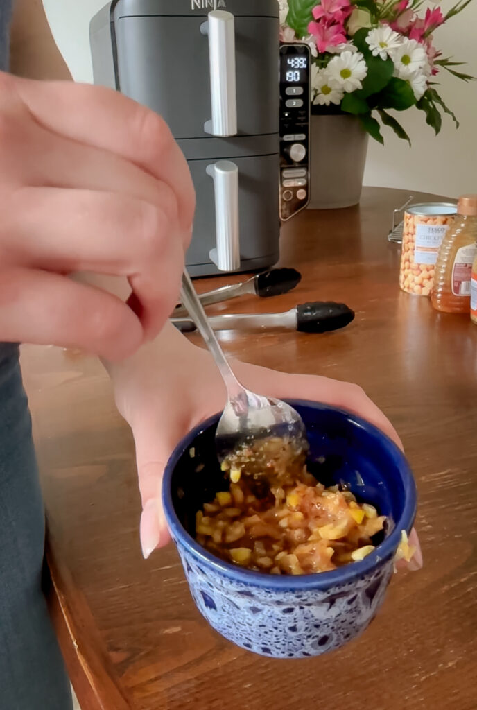 A person using a spoon to mix mashed charred lemon flesh and ingredients into a smooth dressing inside a small blue bowl.