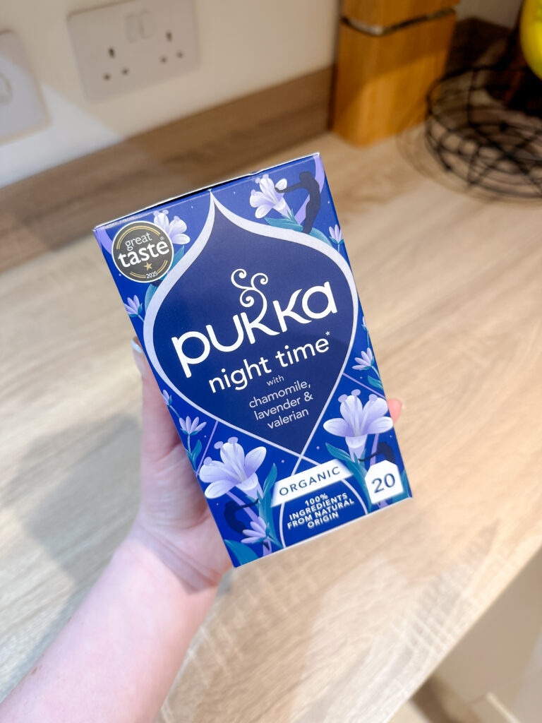 Hand holding a box of Pukka Night Time organic herbal tea in a kitchen