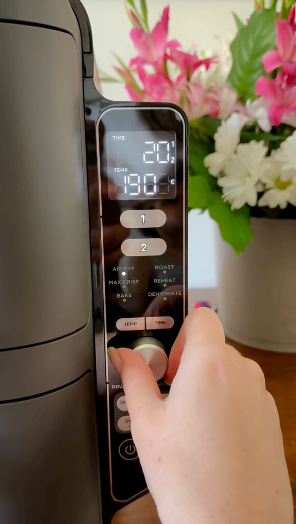 A close-up of a hand turning the control dial on a Ninja air fryer digital display, set to 190 degrees Celsius for 20 minutes.