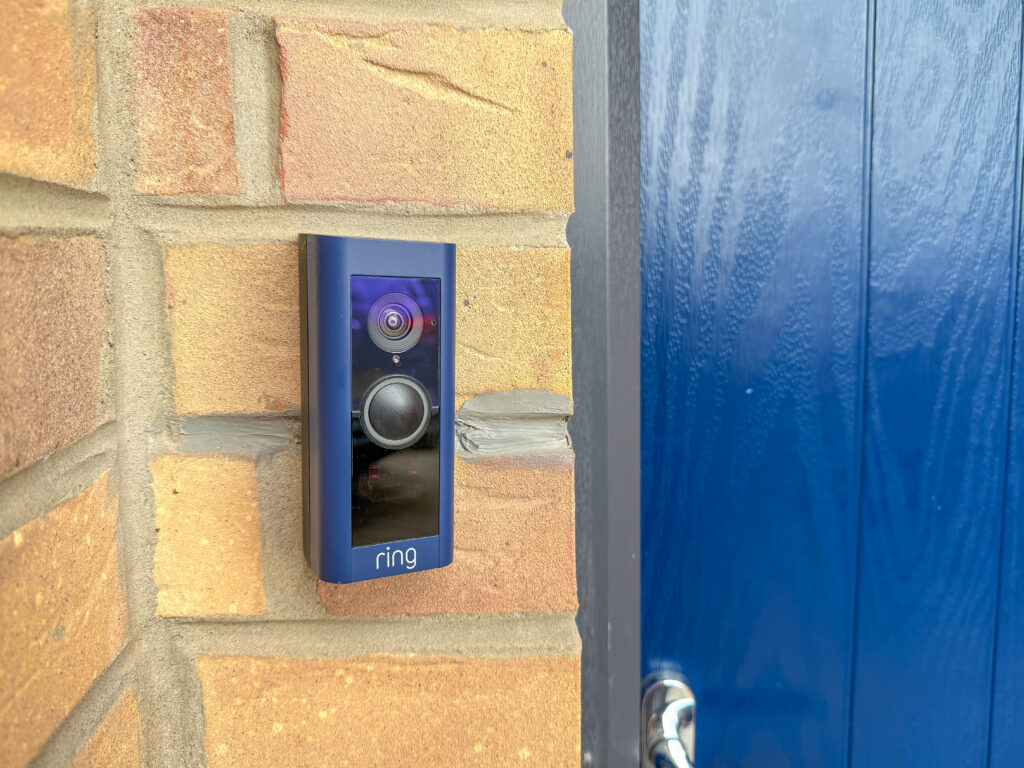 Blue ring video doorbell wired into a house next to a blue front door