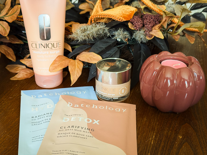 Clinique Moisture Surge body hydrator and face cream next to two Patchology mud mask sachets on a wooden table