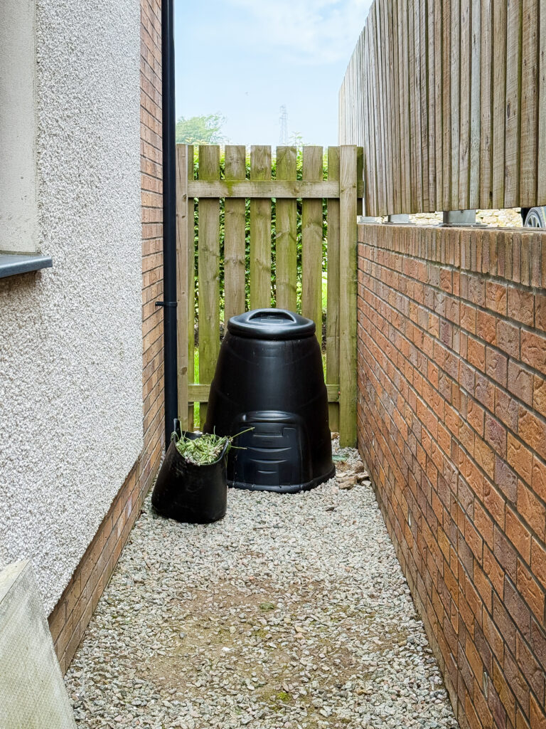 a black compost bin down the side of a house