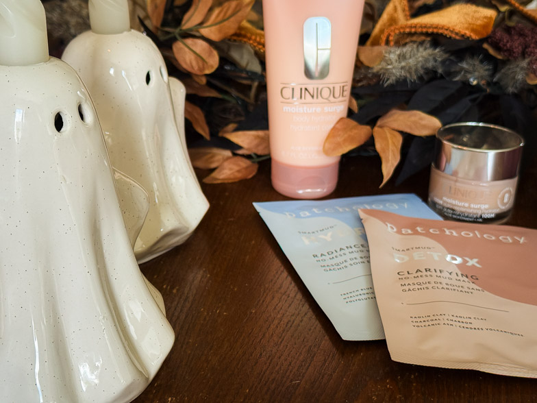 Ceramic ghost candle holders beside Clinique Moisture Surge skincare and Patchology mud mask sachets with autumn foliage