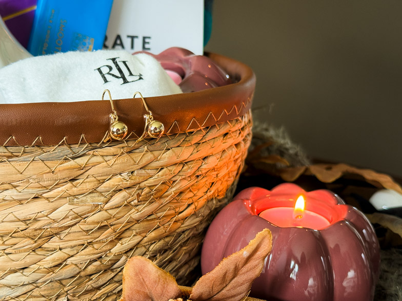 Gold Lauren Ralph Lauren drop earrings hooked over the rim of a woven basket beside a lit pumpkin tealight holder