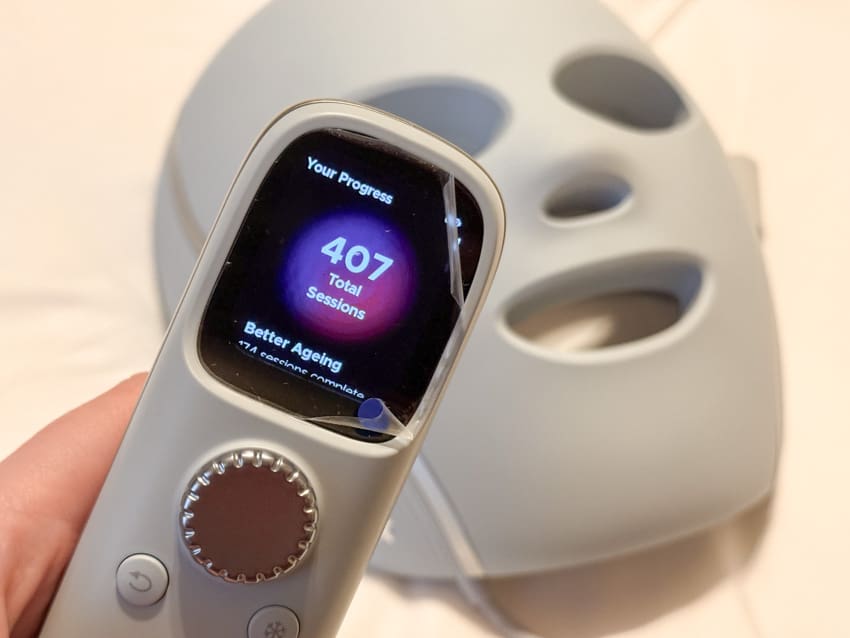Shark CryoGlow controller showing 407 total sessions, held in front of the grey LED face mask.