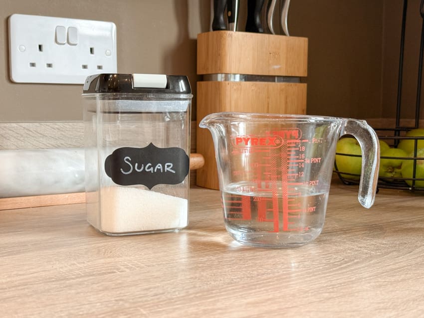 Sugar in a labelled container beside a measuring jug of water, ready to make simple syrup